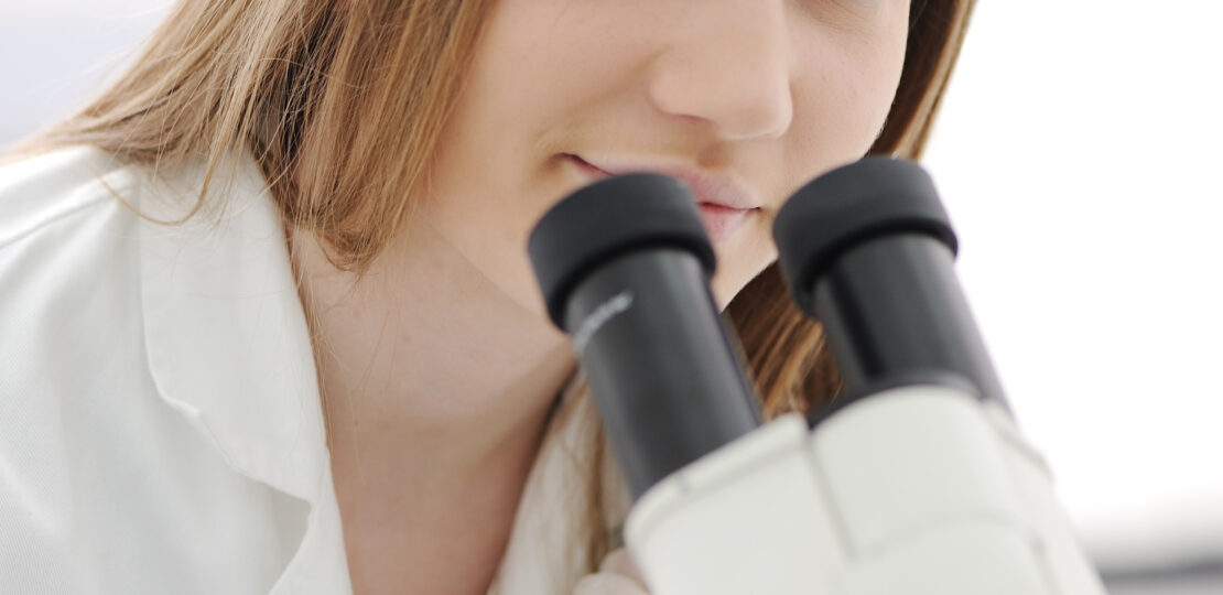 Beautiful female researcher using a microscope in a lab, closeup